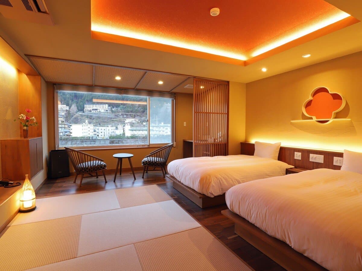 Warmly lit twin room with lounge chairs beside a panoramic window over the valley, Yamagataya, Gero Onsen