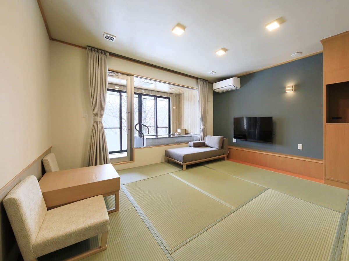Tatami guest room with lounge sofa and private in-room bath overlooking snowy woods at Okunikko Hotel Shikisai