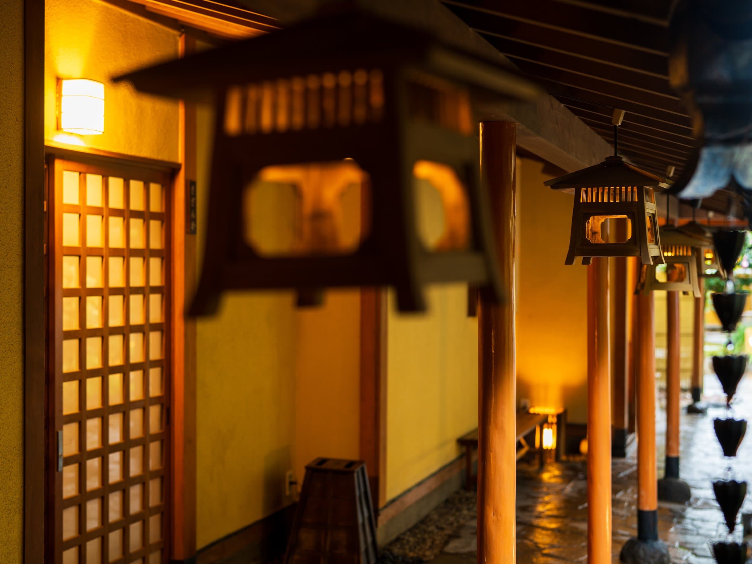 Warmly lit exterior corridor lined with hanging wooden lanterns and shoji screens at night, Kappo Ryokan Kannawa Bettei, Beppu Onsen