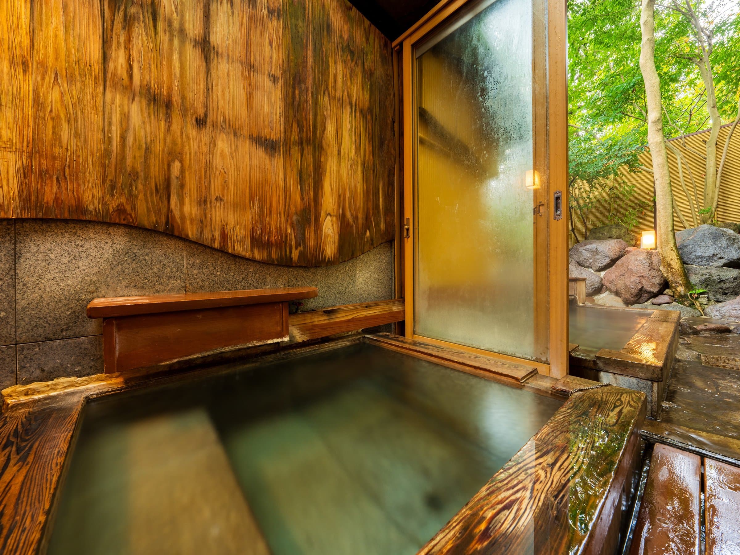 Private cedar-walled bath with stone tub opening onto a lantern-lit rock garden, Kappo Ryokan Kannawa Bettei, Beppu Onsen