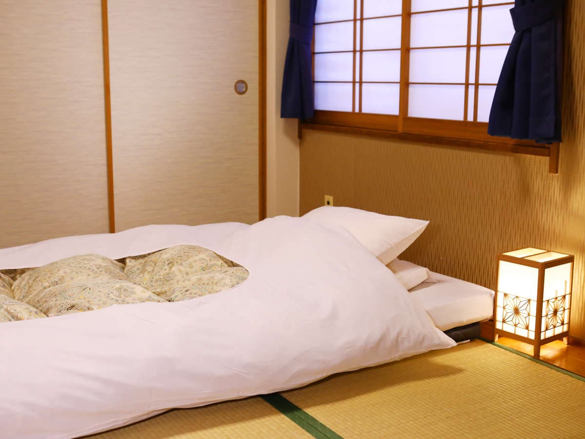 Atmospheric futon bedding detail at Ryokan Kamogawa Asakusa with a glowing washi andon lamp beside a tatami floor