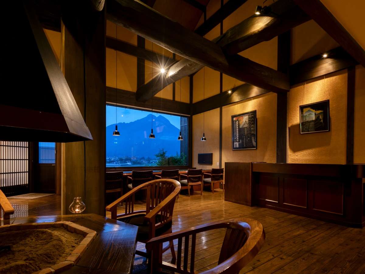 Timber-framed lounge with sunken hearth at Tosyoan, lit at dusk with Mount Yufu visible through the picture window