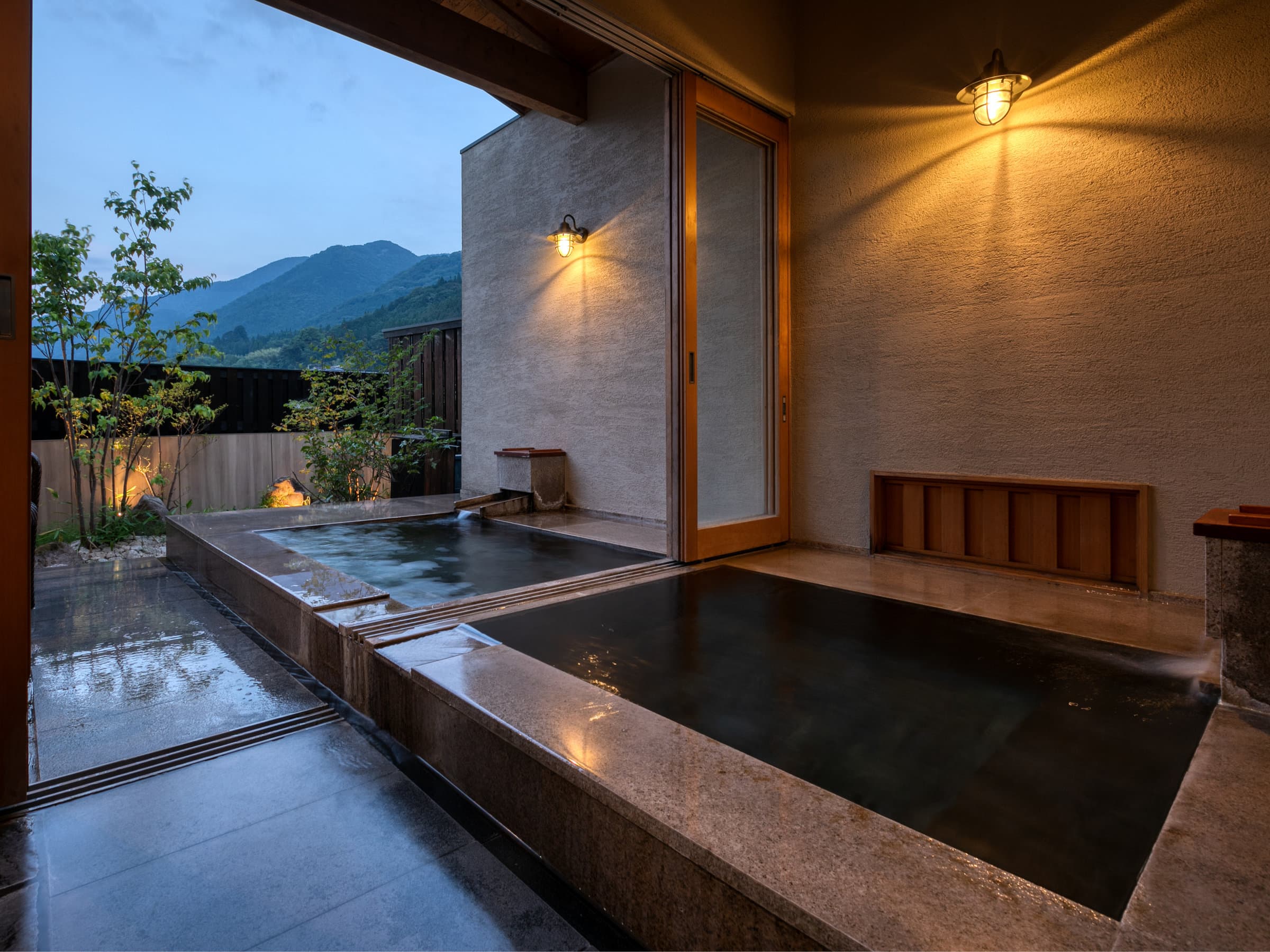 Private open-air stone rotenburo bath at Tosyoan glowing at dusk with a lantern and mountain backdrop