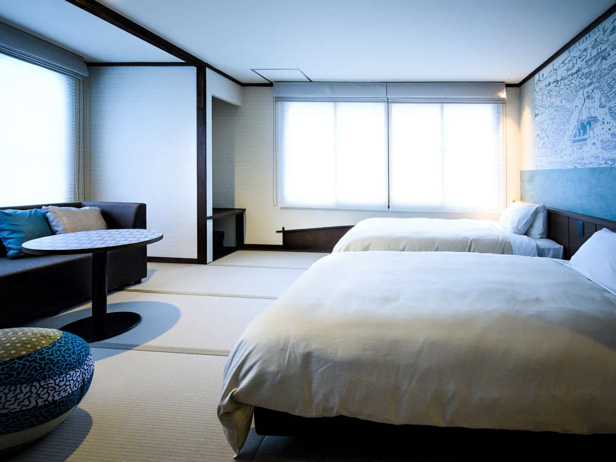Bright tatami guest room with twin low beds, sofa and round table by shaded windows