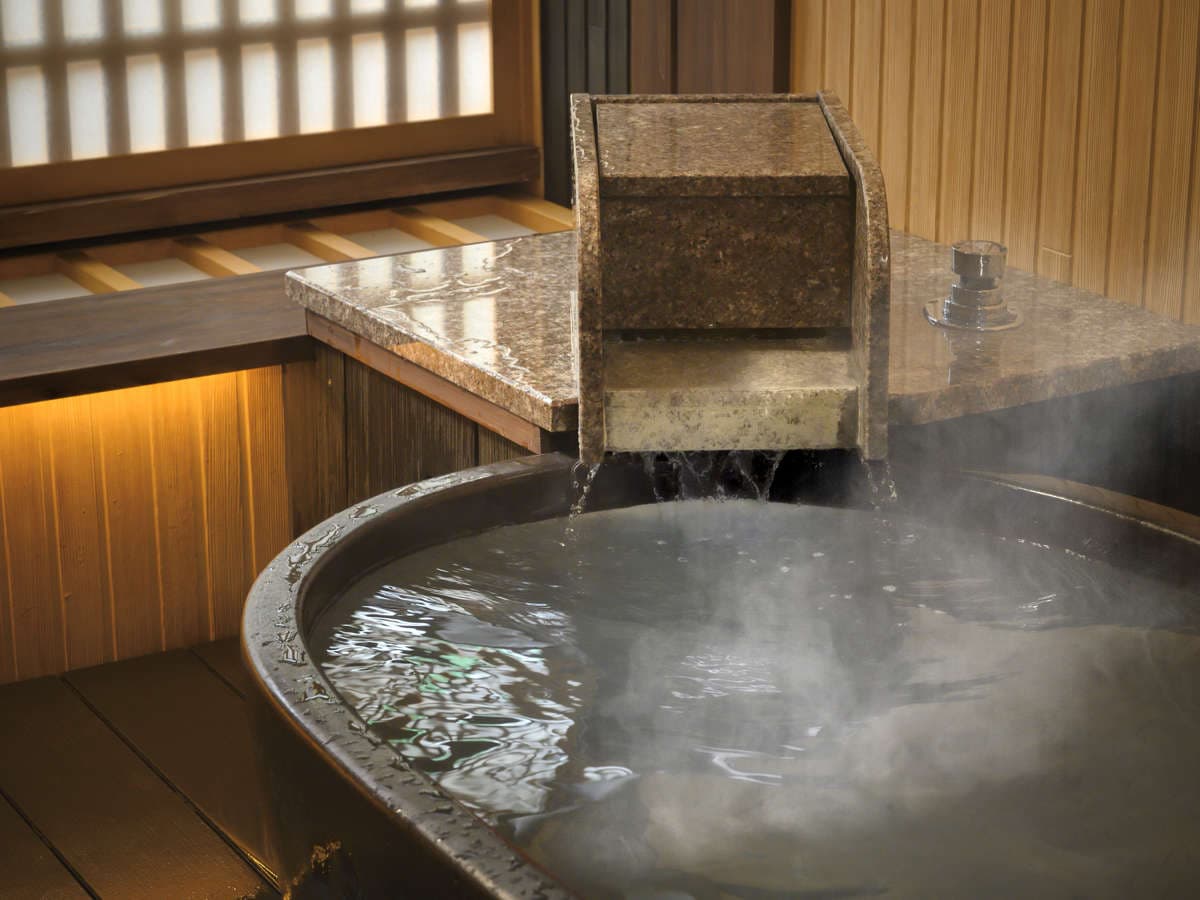 Round private bath with stone spout pouring steaming spring water beside a wood-panelled wall