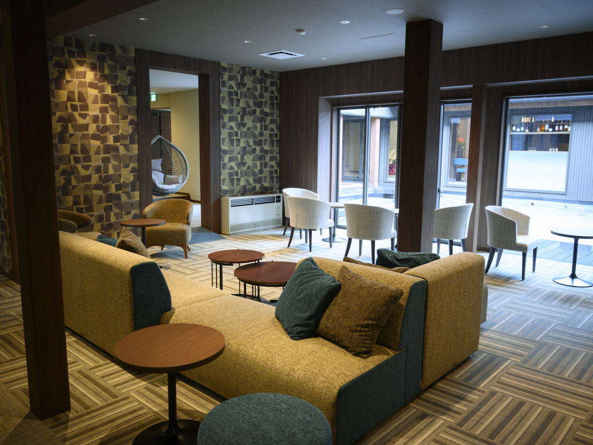 Wide lounge with patterned feature walls, sofas, hanging chair and tub chairs by glass doors
