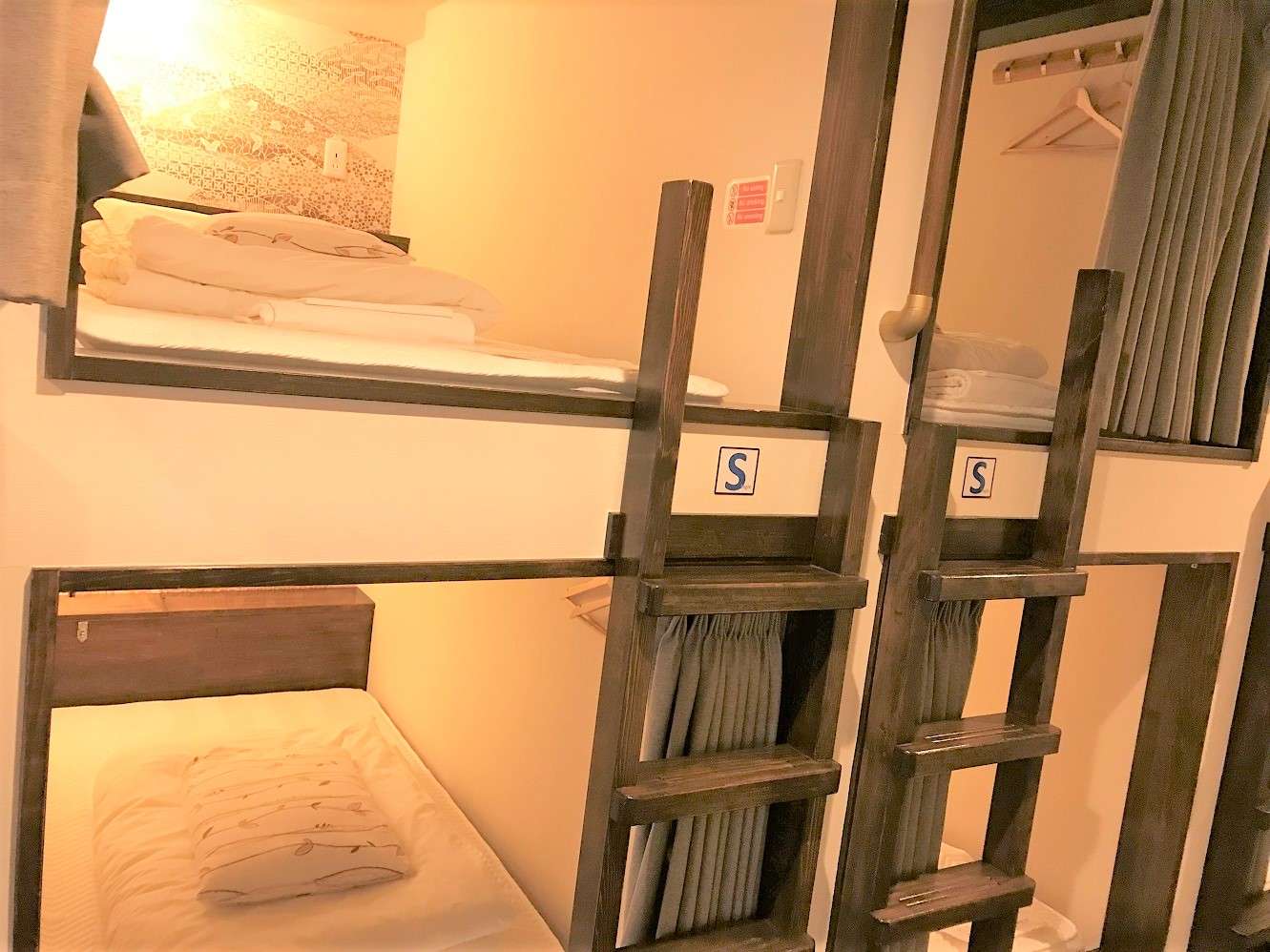 Wooden bunk-bed dormitory beds with privacy curtains and ladders