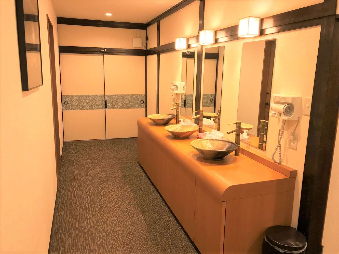 Shared washroom vanity with ceramic bowl basins, mirrors and warm lighting