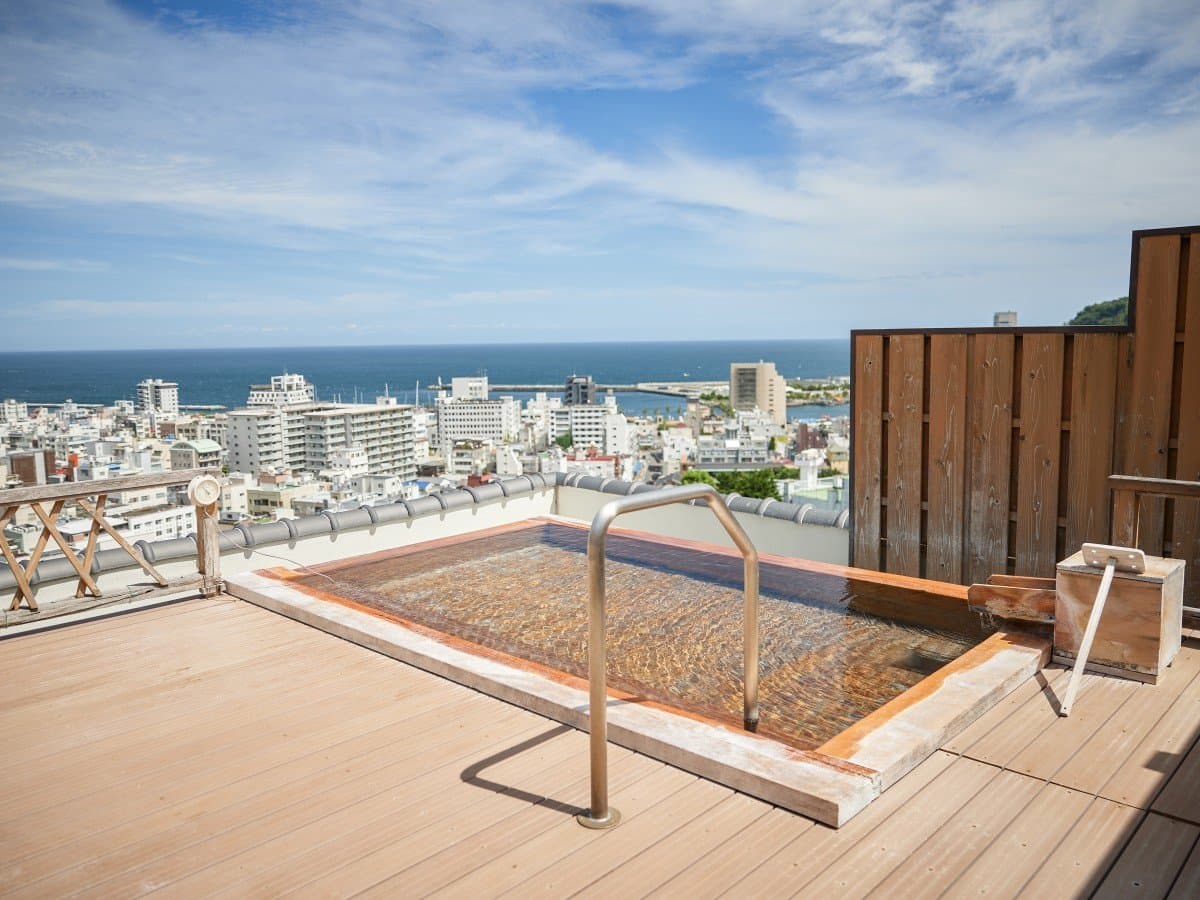 Rooftop open-air hot spring bath at Atami no Yu Shin Kadoya overlooking Atami townscape and the sea on a clear day
