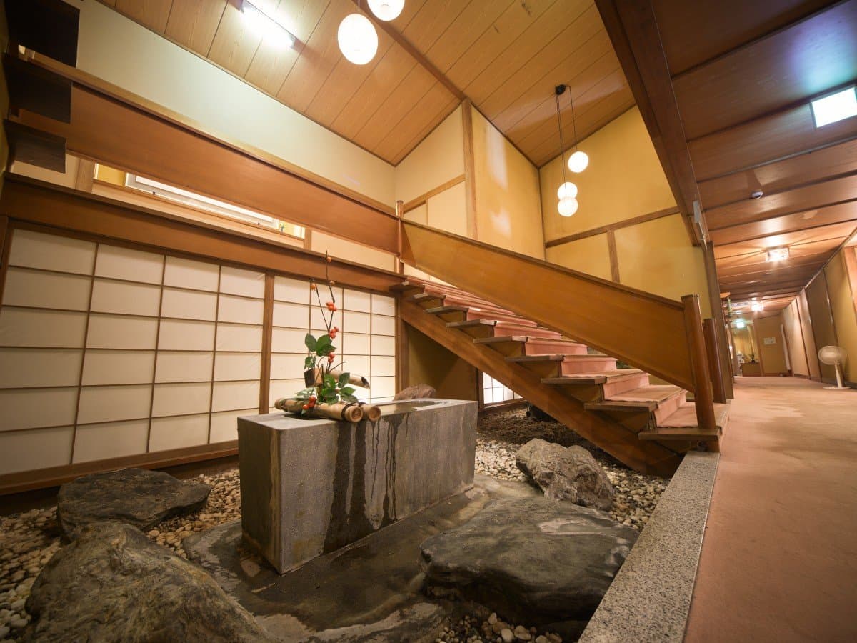 Interior of Shin Kadoya in Atami with a stone water basin, wooden staircase and shoji-screened lobby