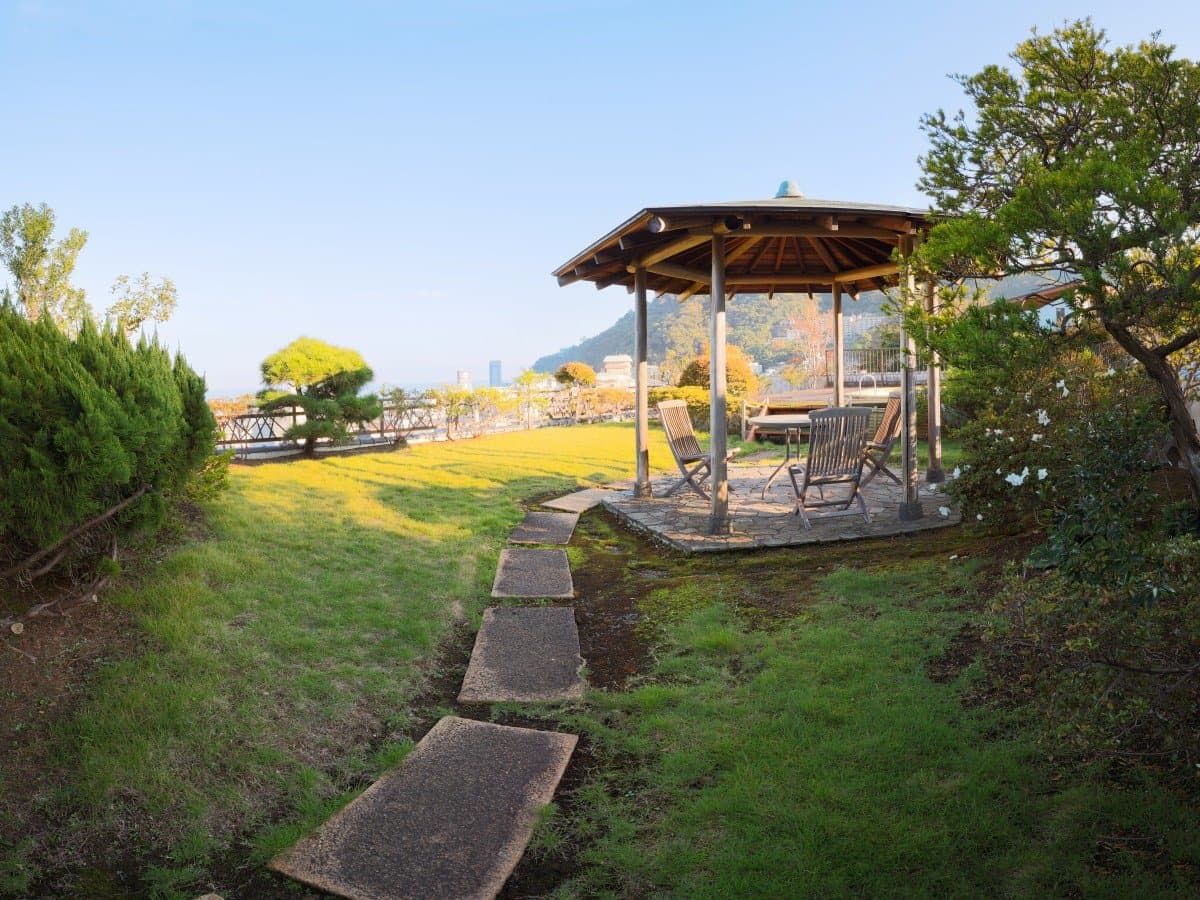 Garden lawn with a wooden gazebo and lounge chairs and distant sea view at Shin Kadoya in Atami