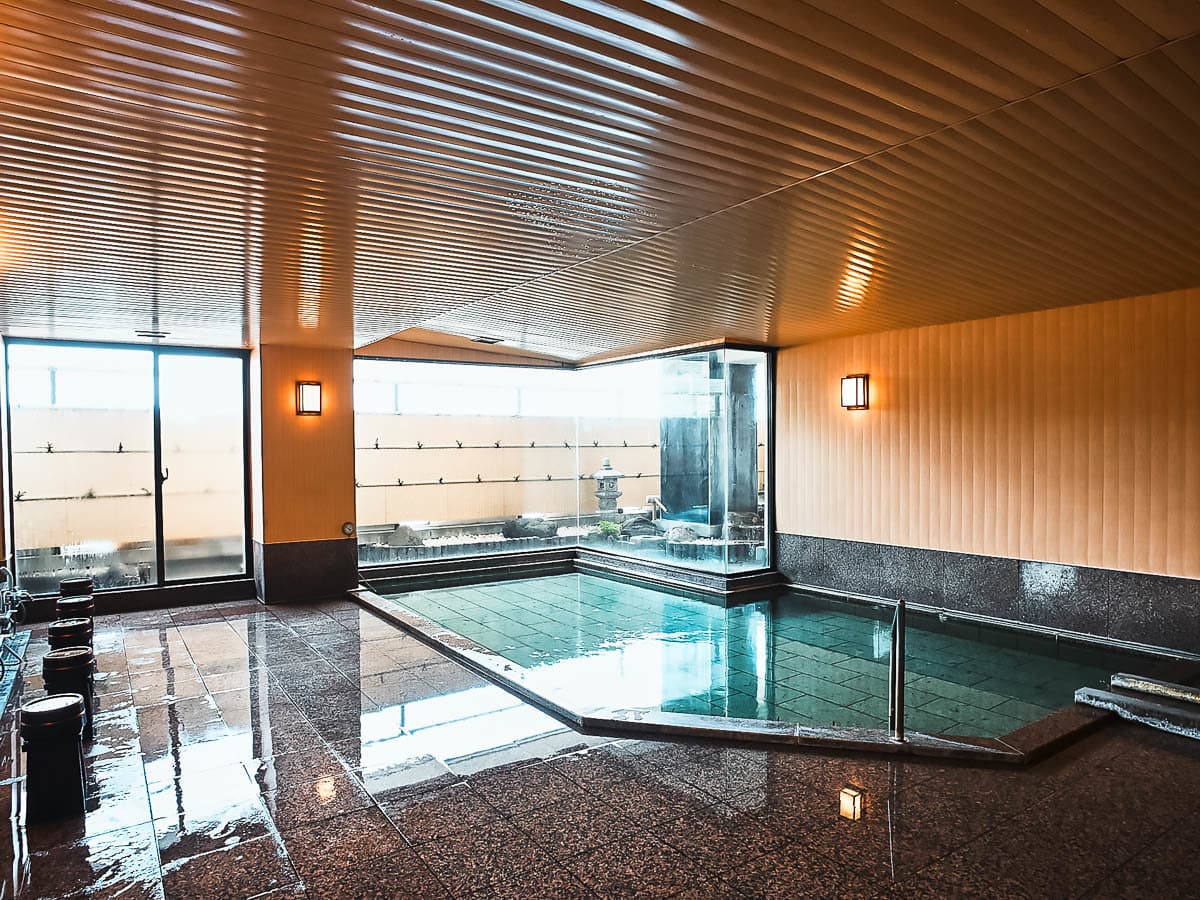 Indoor stone hot spring bath with large windows and warm lighting at Shin Kadoya in Atami