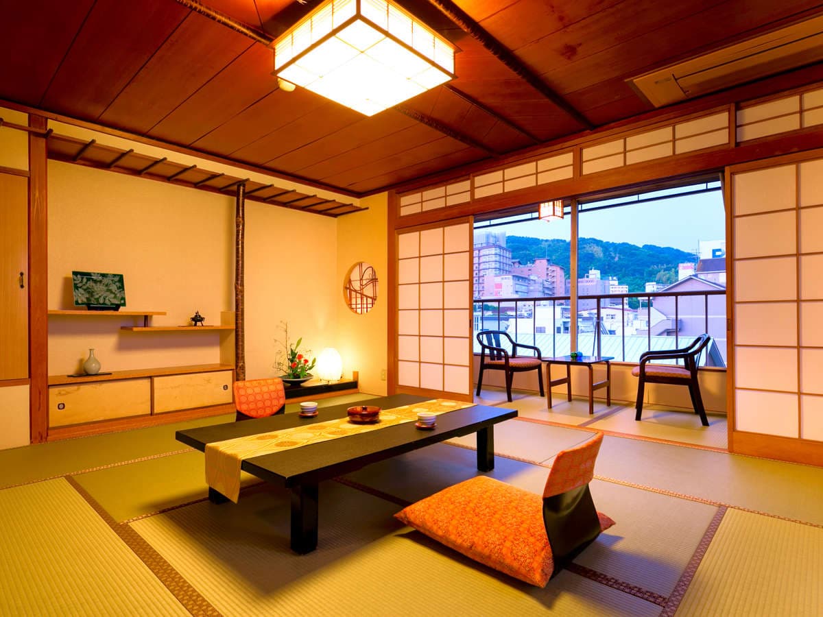 Warmly lit tatami guest room with balcony seating and Matsuyama town view at Dogo Grand Hotel