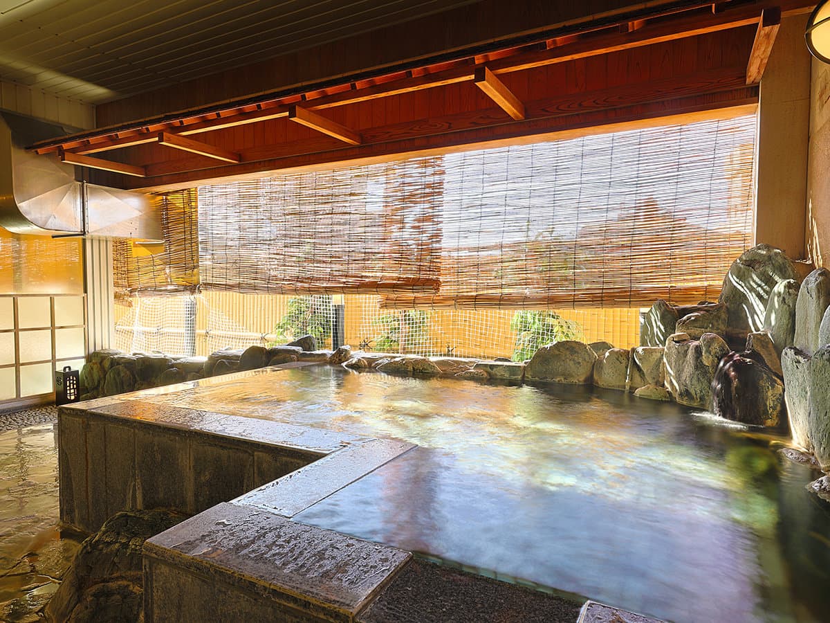 Rock-rimmed open-air hot spring bath with bamboo screen and garden view at Dogo Grand Hotel