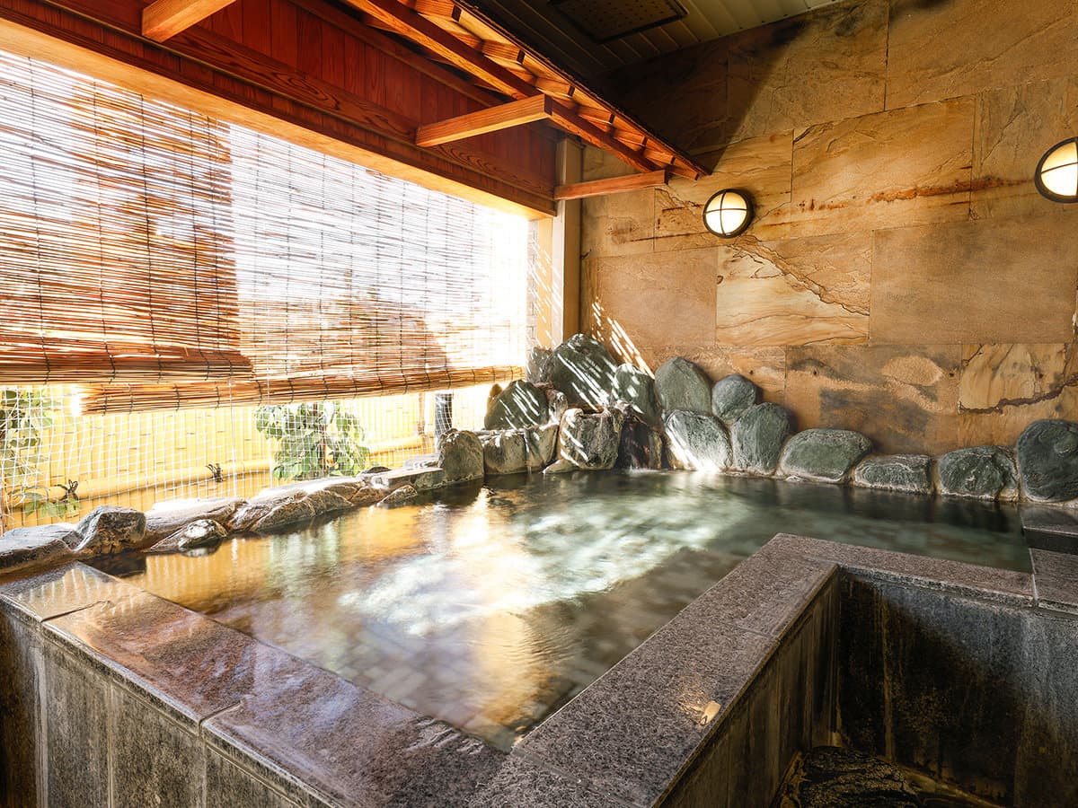 Stone outdoor onsen bath framed by natural rock wall and bamboo blinds at Dogo Grand Hotel