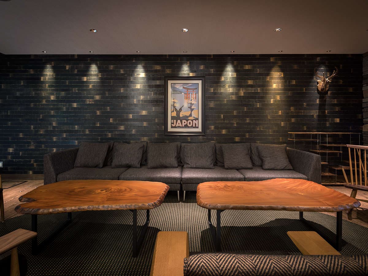 Lounge at Hotel Miyajima Villa with dark wood wall, live-edge tables and grey sofa