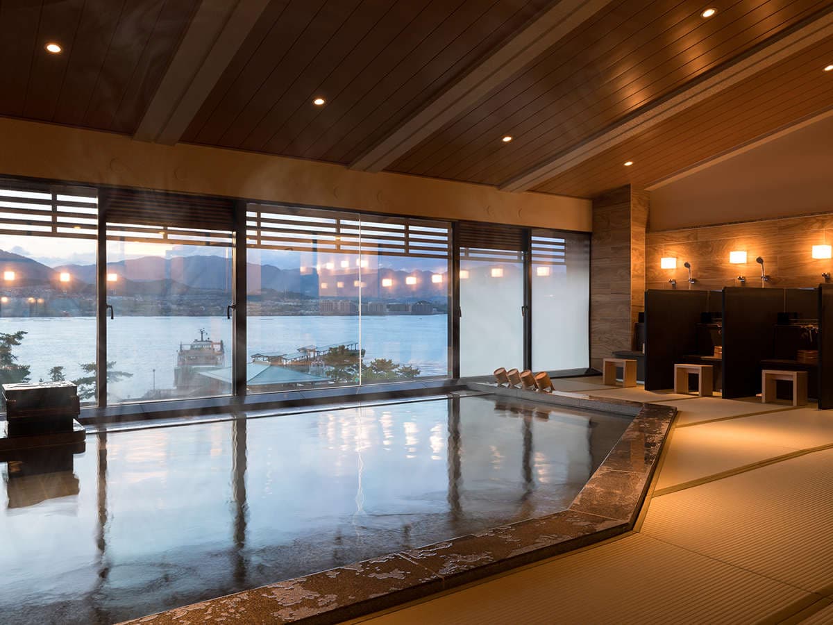 Tatami-floored indoor hot spring bath overlooking the sea and ferry pier at Hotel Miyajima Villa