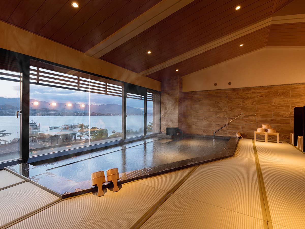 Indoor onsen bath with rising steam and panoramic Seto Inland Sea view at dusk, Hotel Miyajima Villa
