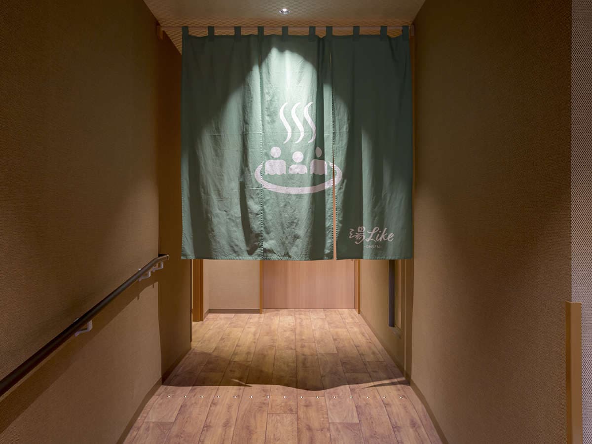 Wood-floored corridor leading to the onsen bath behind a green noren curtain at Hotel Miyajima Villa