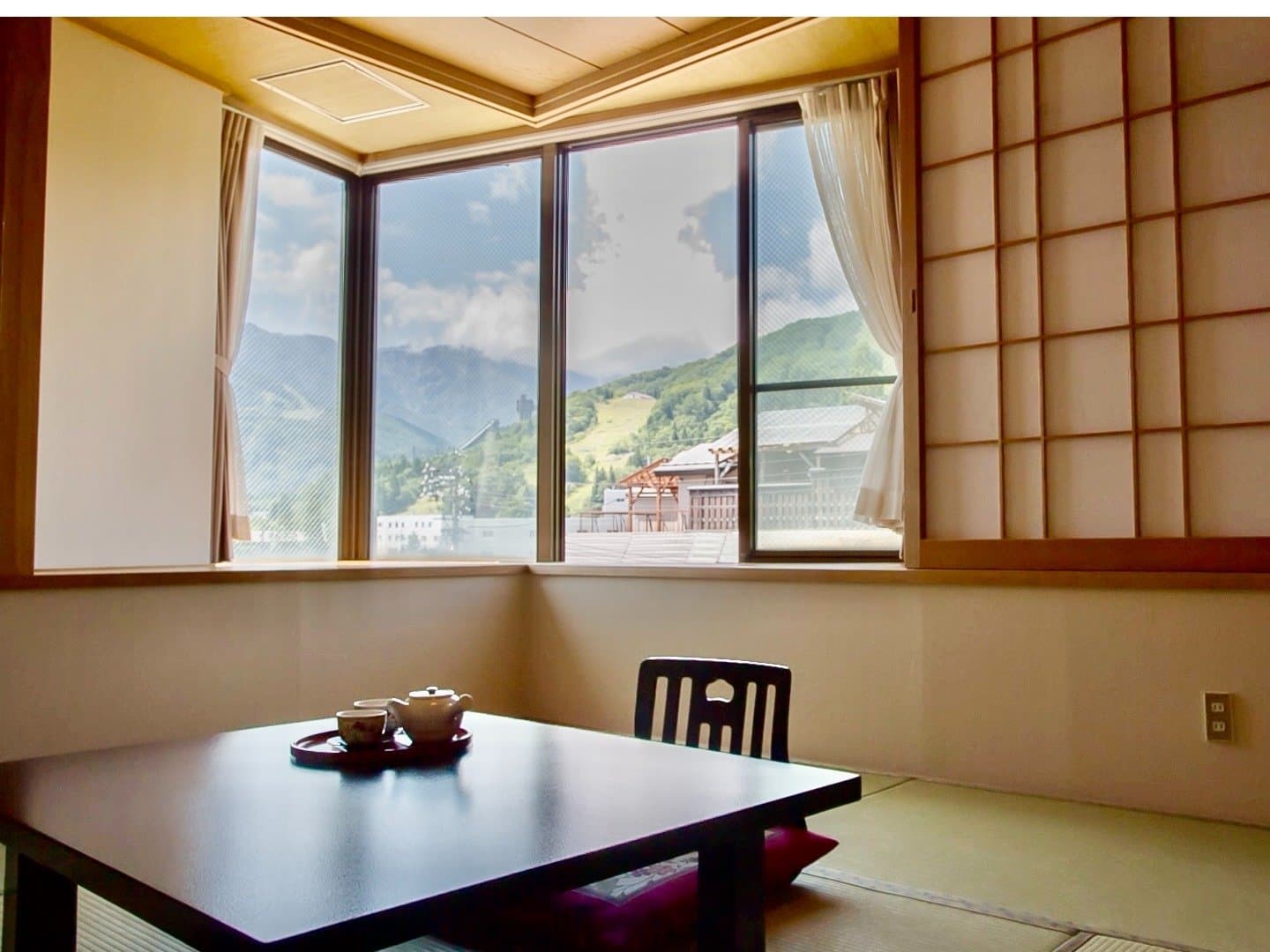 Tatami guest room with a low tea table and corner windows framing the Happo-one mountains and ski slopes of Hakuba