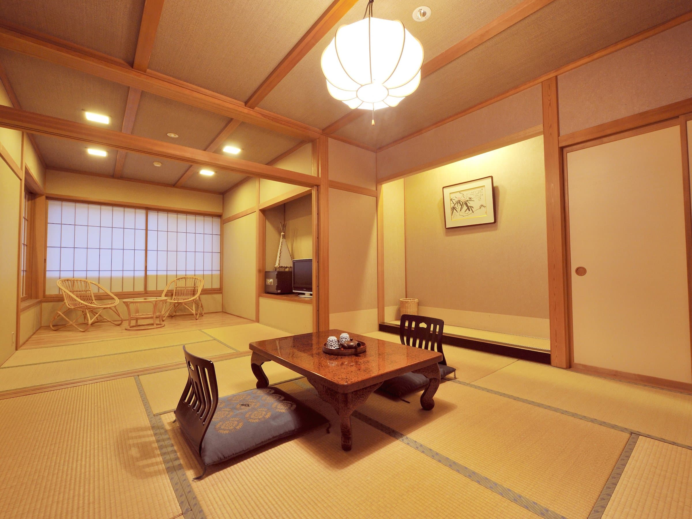 Spacious tatami guest room with a hiroma seating nook and rattan chairs by the shoji windows at Shirouma-so in Hakuba