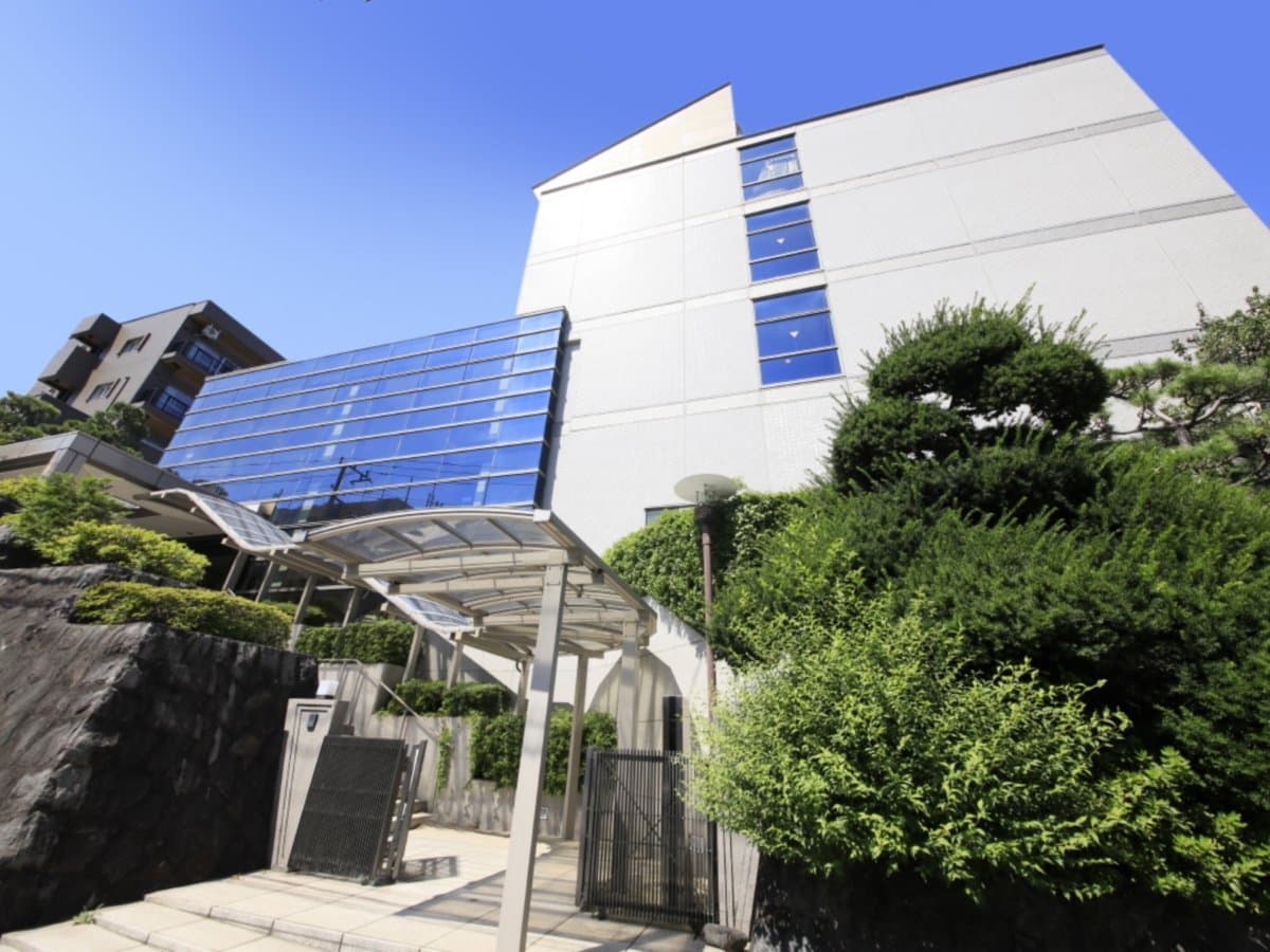 Atami Fuga onsen hotel exterior under a clear blue sky, with the entrance gate, pines and hillside greenery in Atami
