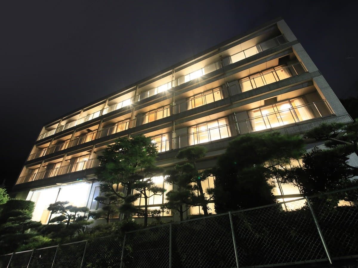 Atami Fuga building illuminated at night, warm-lit guest room windows above landscaped pine garden