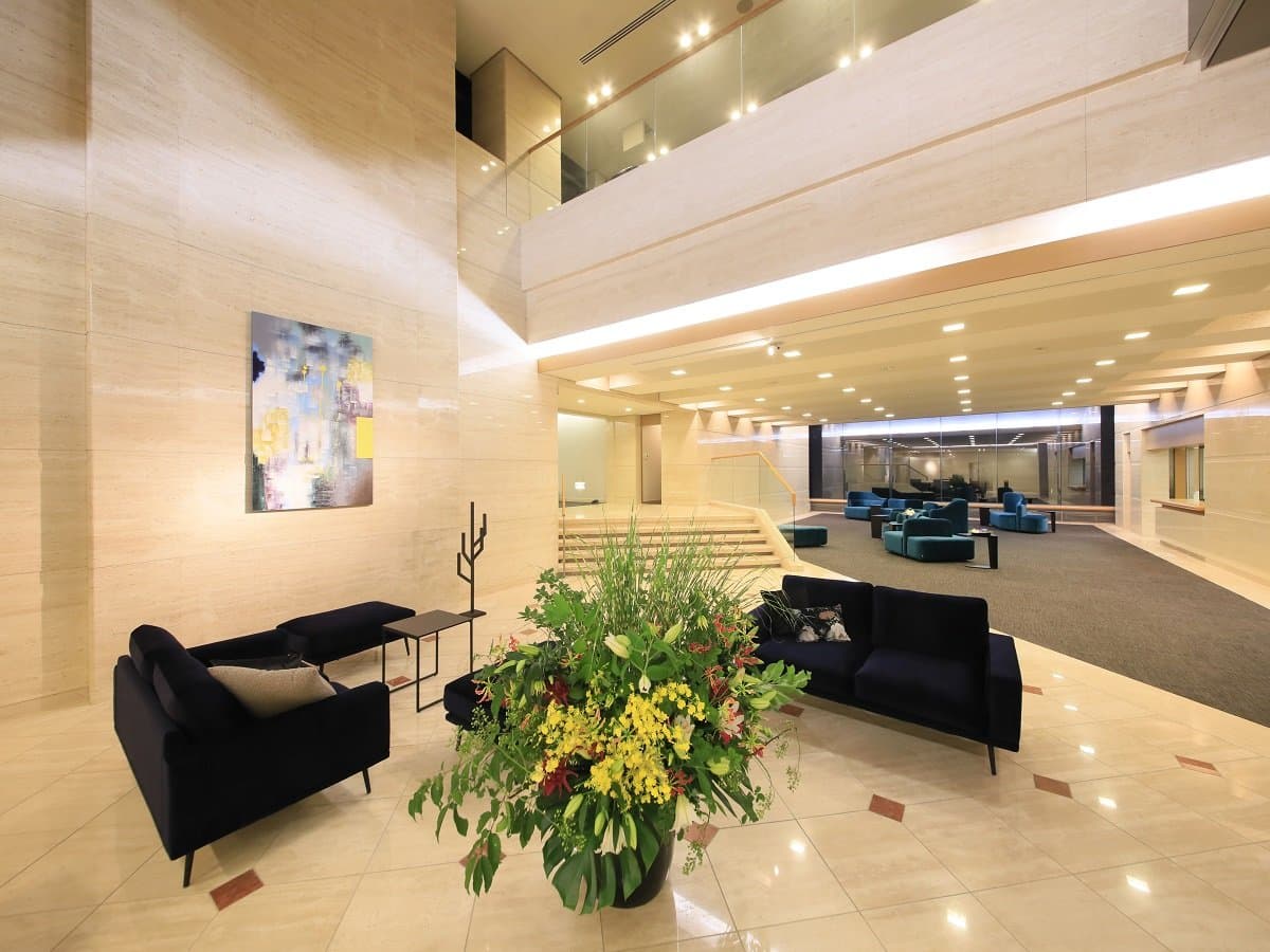 Spacious stone-floored lobby lounge at Atami Fuga with navy sofas and a large seasonal floral arrangement