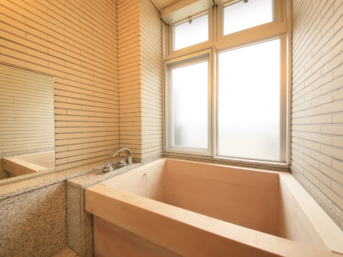 Private cypress wood bathtub in a guest room at Atami Fuga set against tiled walls and a frosted window