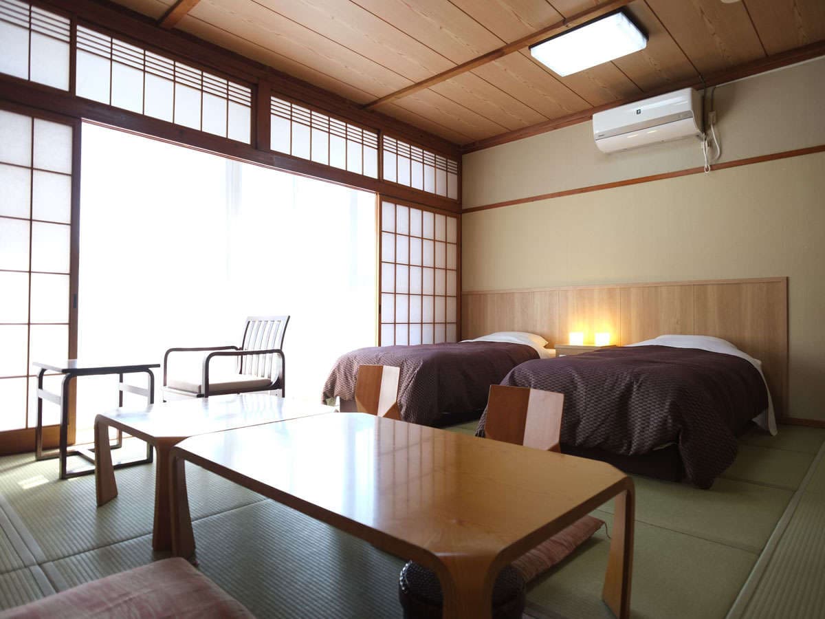 Tatami guest room with twin beds, low table and large bright window at Hotel Harumoto in Nikko