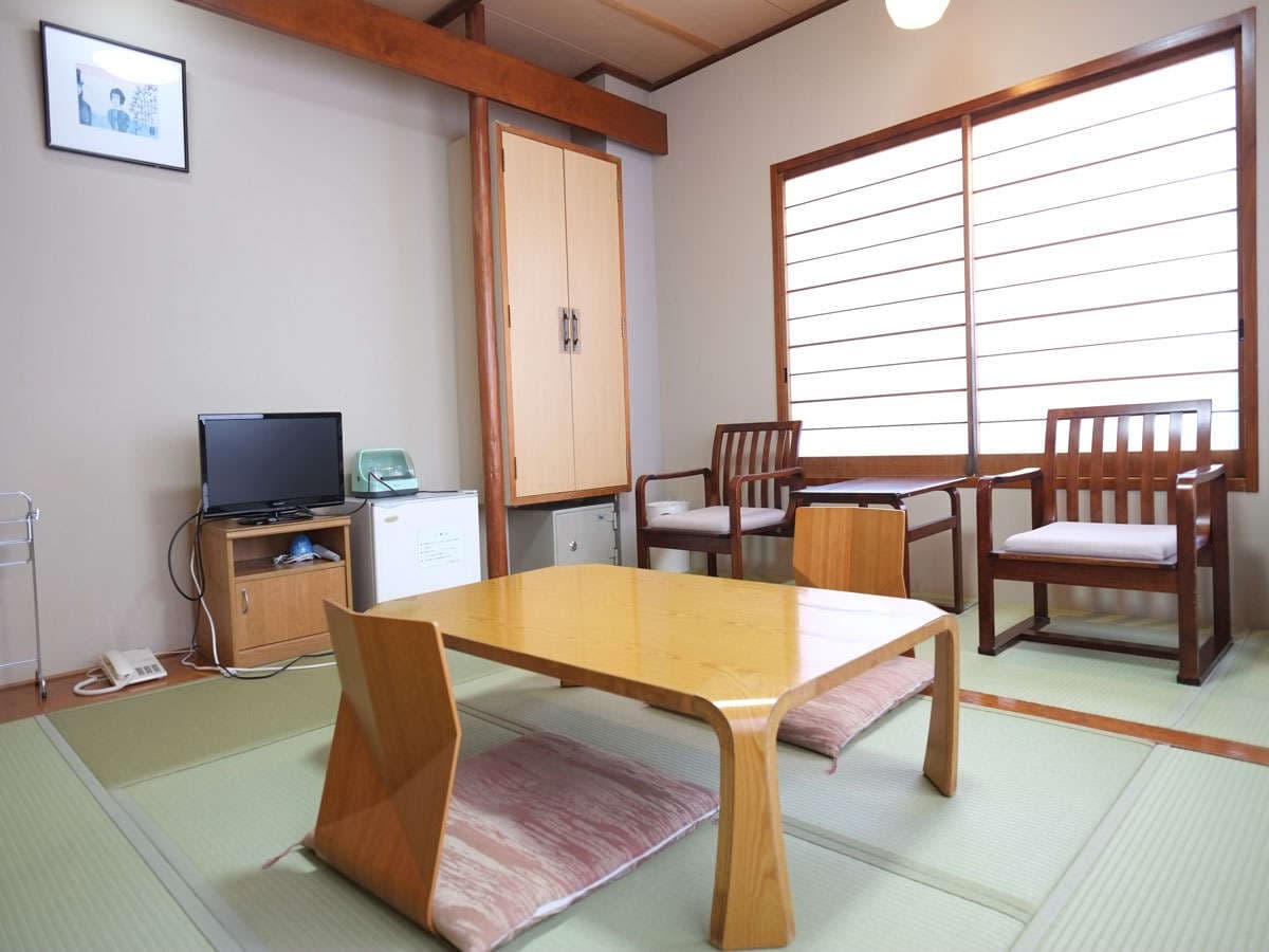 Compact Japanese-style room with tatami flooring, wooden table and armchairs by a shoji window at Hotel Harumoto