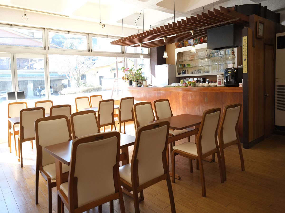 Bright dining hall and lounge with wooden tables and chairs beside large windows at Hotel Harumoto in Nikko