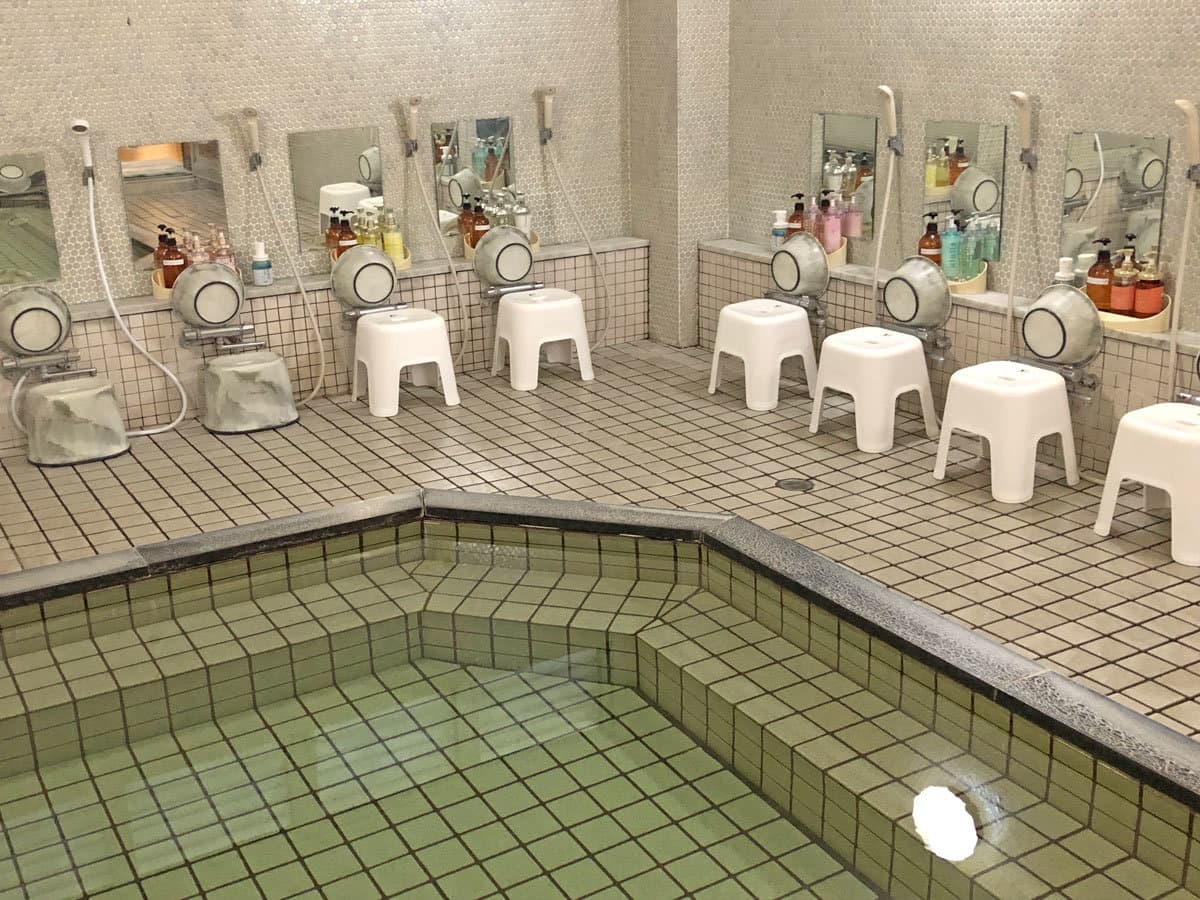 Indoor public bath with green-tiled soaking tub and tiled washing stations at Hotel Harumoto in Nikko