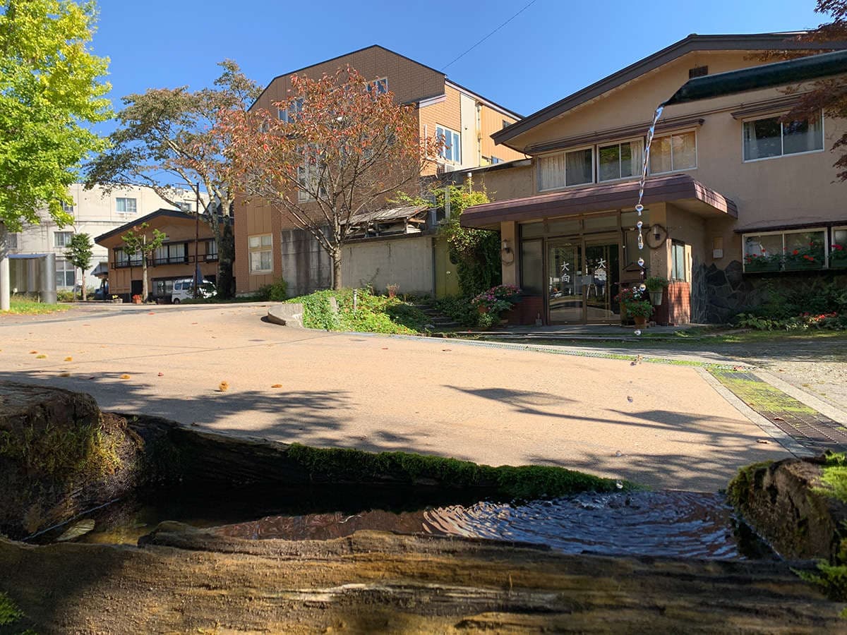 Oomukou Ryokan exterior on a clear day with a garden stream in front, Happo Onsen, Hakuba