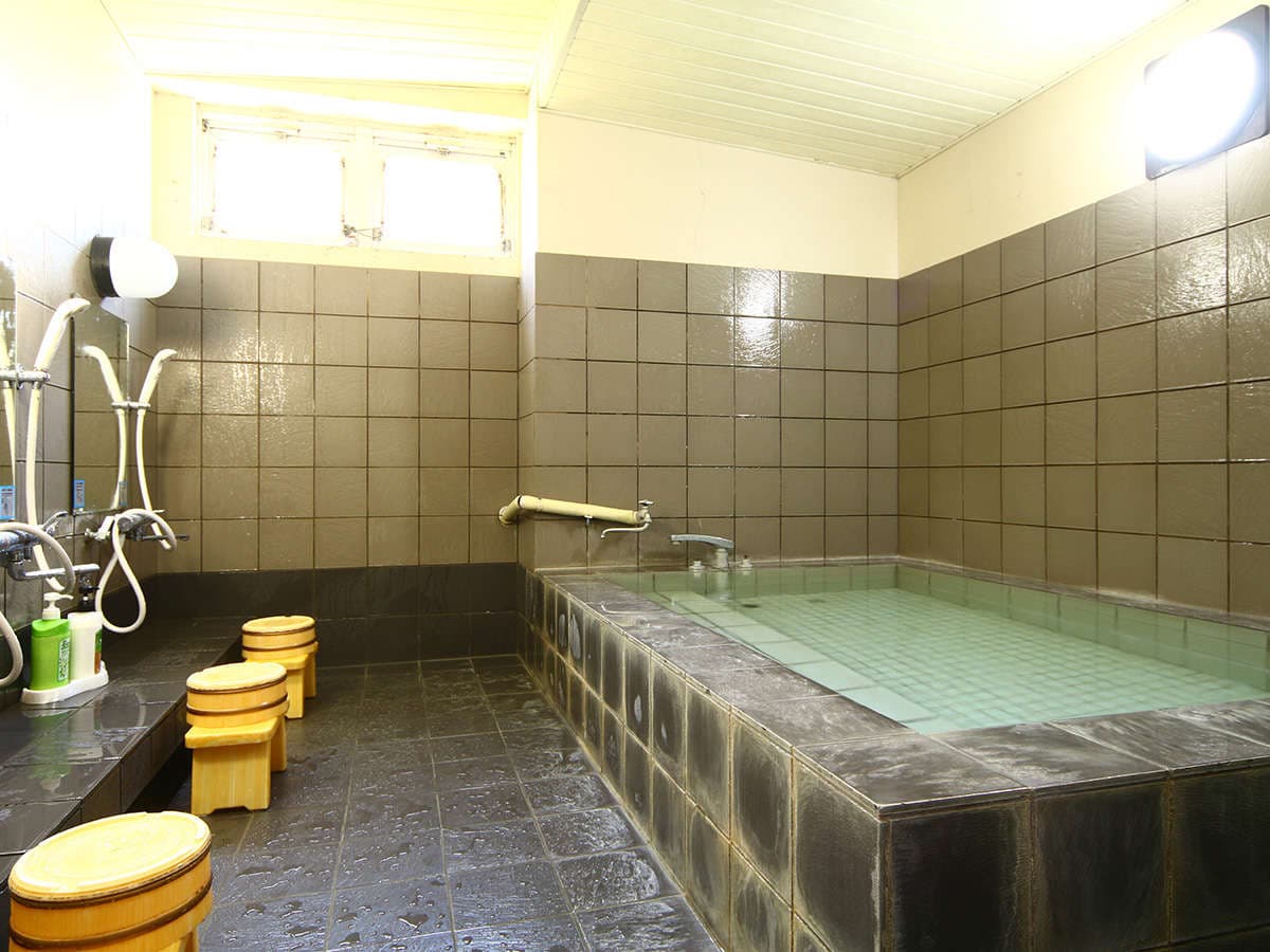 Indoor hot spring bath at Oomukou Ryokan with a tiled tub, washing stations and wooden stools