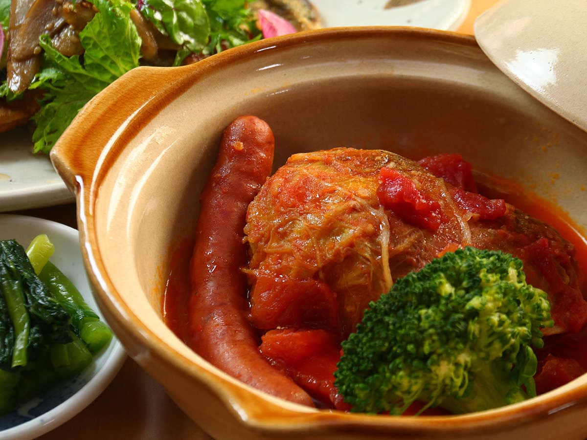 Hearty tomato-stewed dinner dish at Oomukou Ryokan served in an earthenware pot with sausage and broccoli