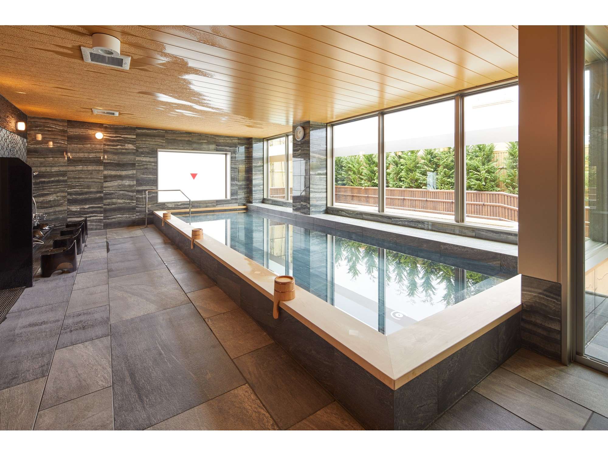 Indoor onsen bath at Wat Hotel & Spa Hida Takayama with stone walls and a large window overlooking greenery