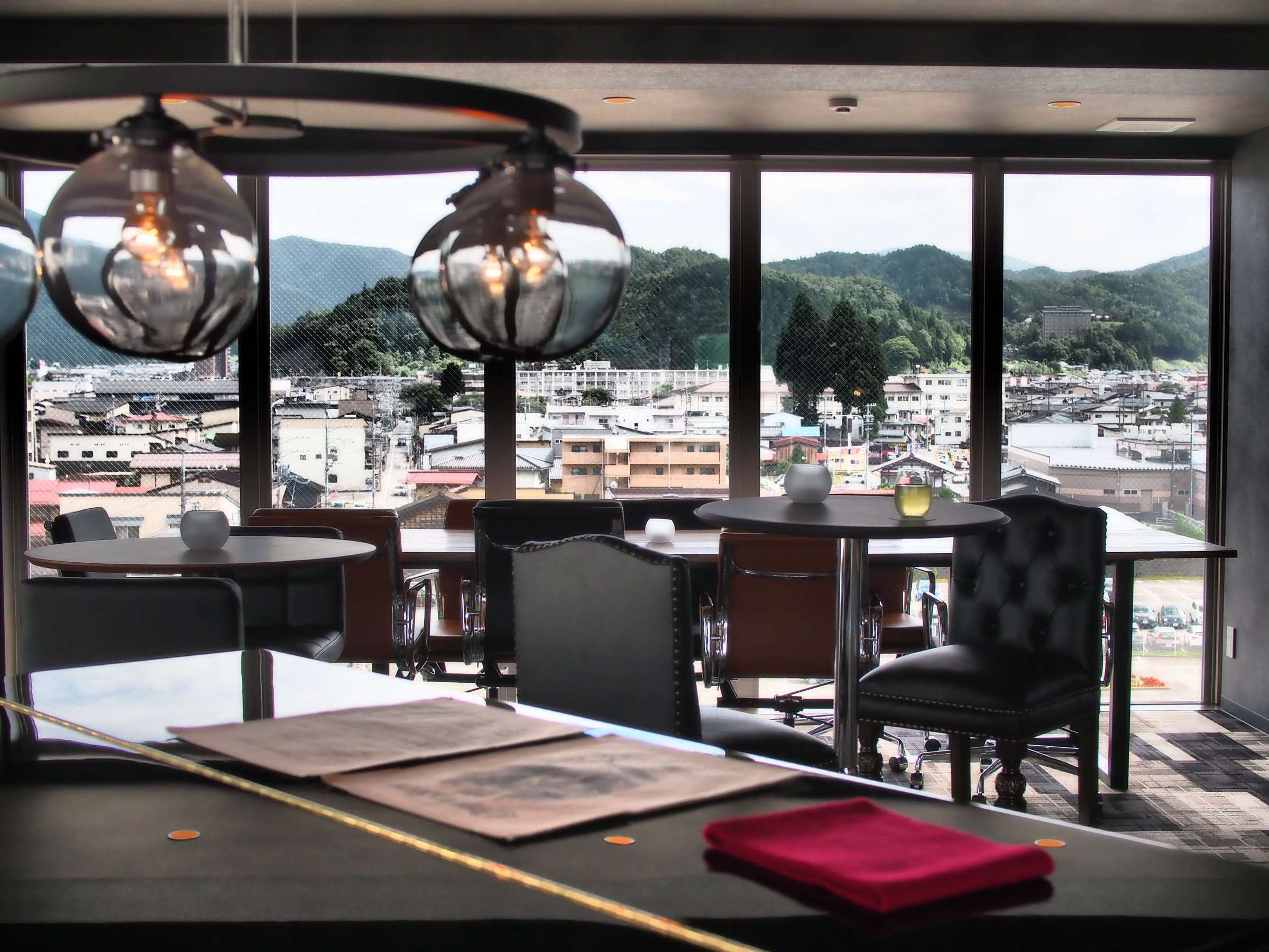 Window-side lounge tables at Wat Hotel Hida Takayama overlooking the Takayama townscape and surrounding mountains