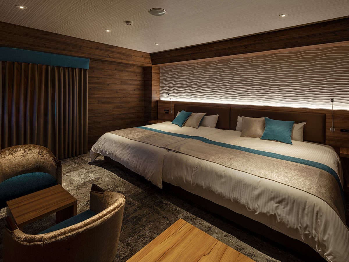 Twin-bed guest room at Wat Hotel Hida Takayama with wood-panel walls, a wavy textured headboard wall and lounge chairs