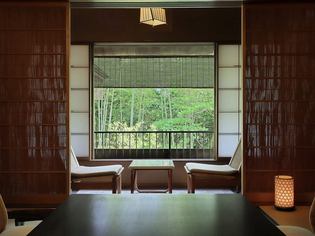 Guest room sitting area framed by reed screens with rattan chairs, andon lantern and a bamboo forest view at Yagyu no Sho, Izu