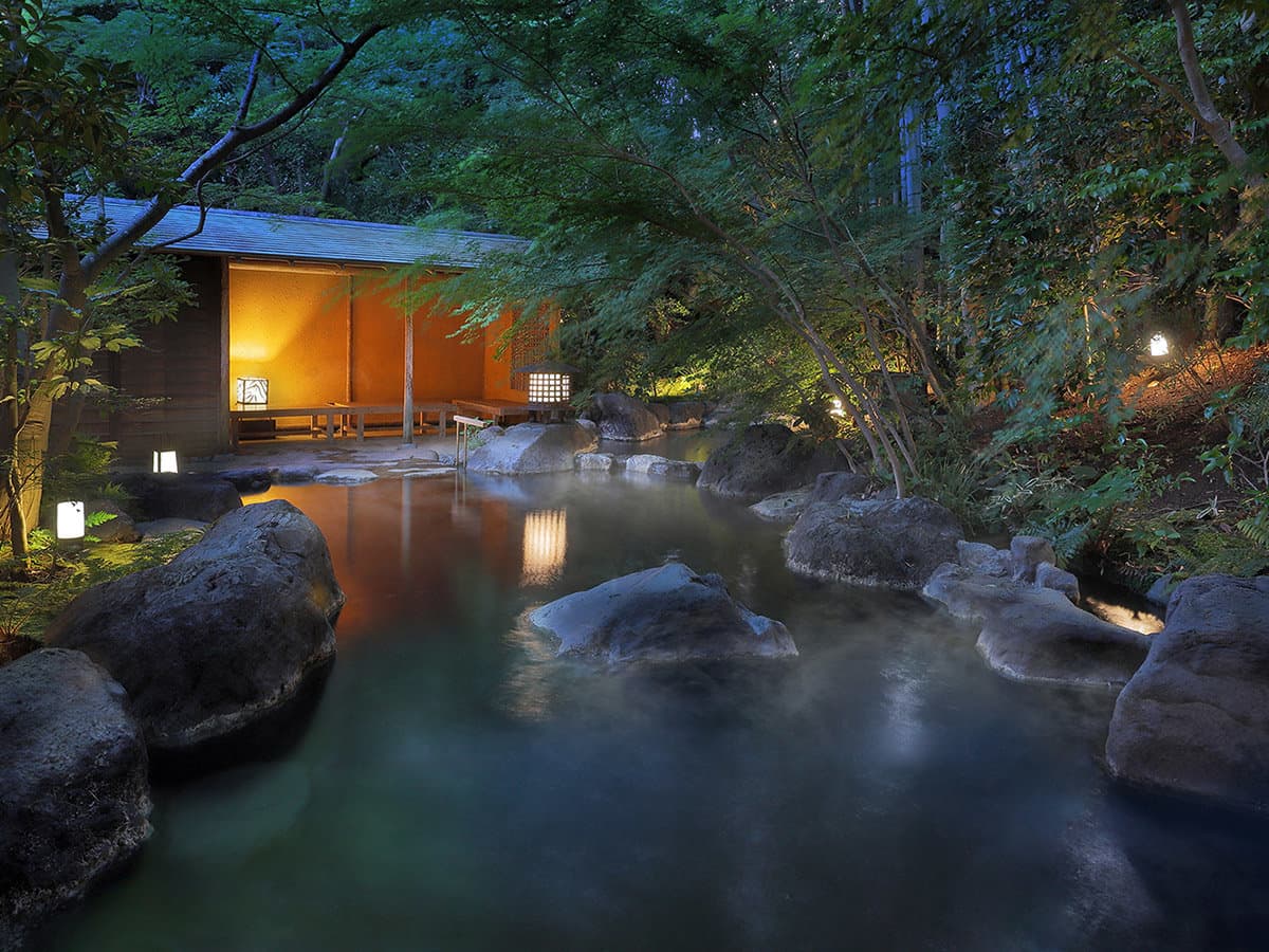 Outdoor rotenburo hot spring at dusk steaming beside a glowing bathhouse and lantern at Yagyu no Sho, Shuzenji Onsen, Izu
