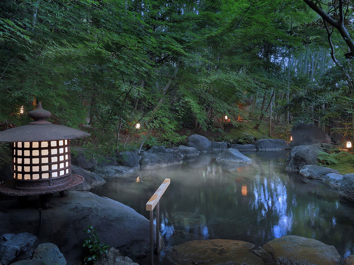 Steaming stone rotenburo open-air bath ringed by rocks, greenery and a stone lantern at dusk at Yagyu no Sho, Izu