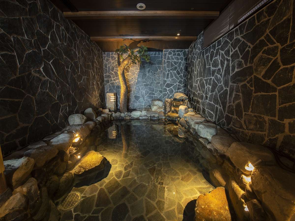Indoor stone communal hot-spring bath with pine tree and warm lighting at Noto Kaishu, Wakura Onsen