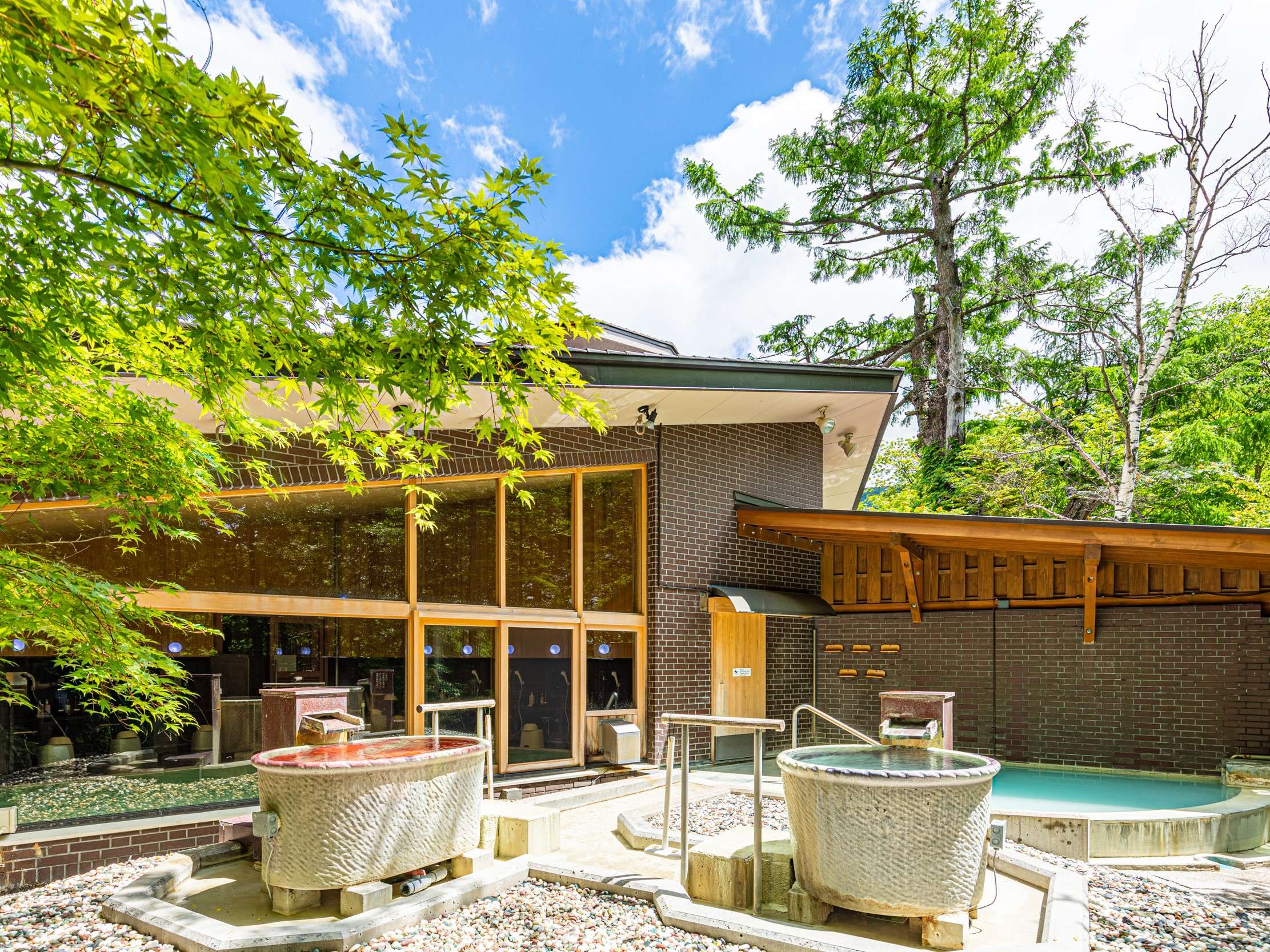 Outdoor bath area with stone tubs and a private rotenburo beside the brick bathhouse and forest