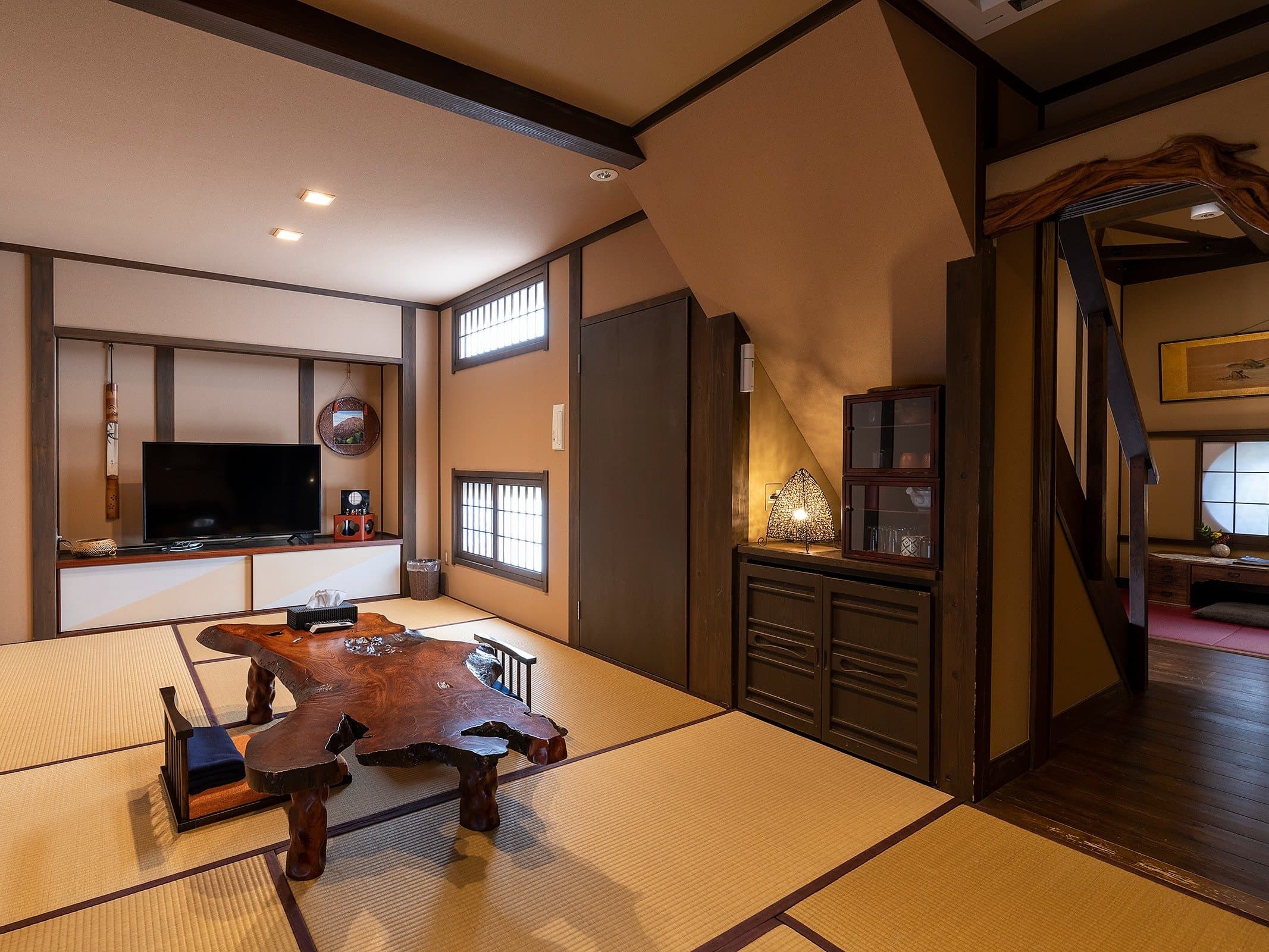 Tatami living area of a guest room at Yado Taniya with low wooden table, TV cabinet and antique chest
