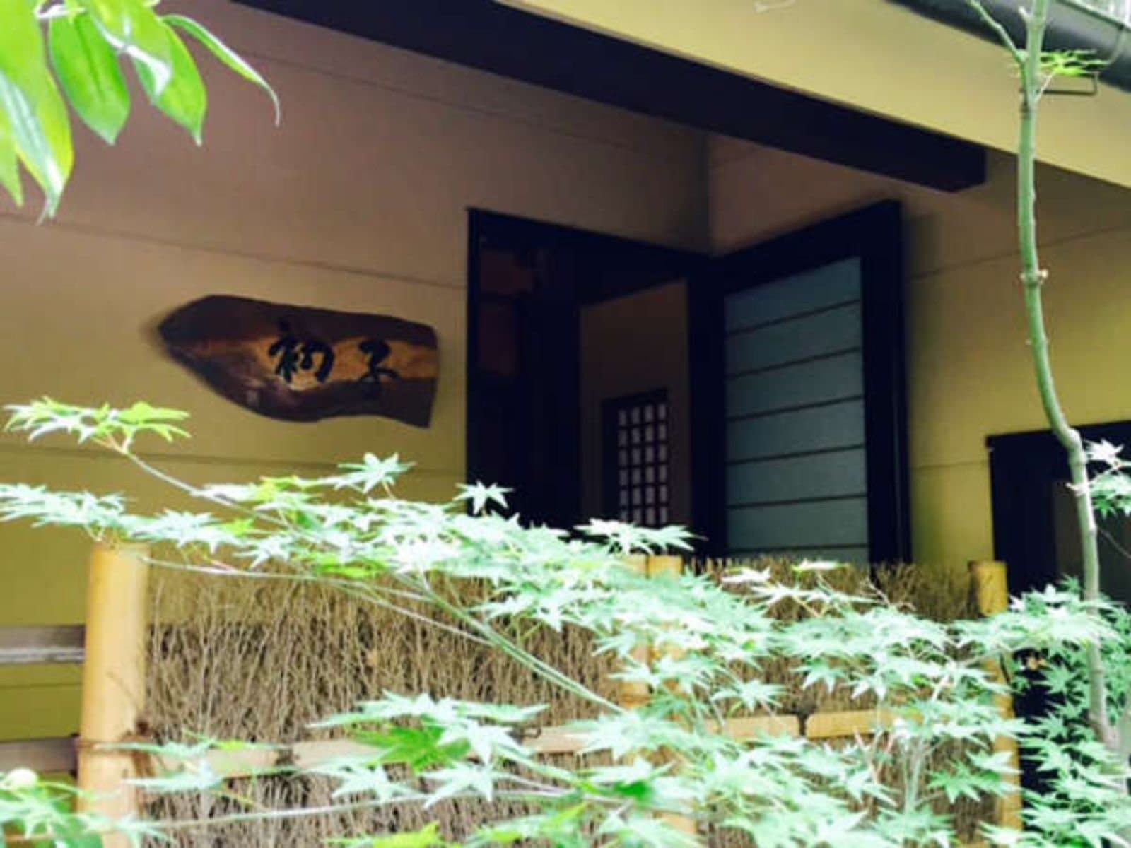 Entrance of Yado Taniya at Dogo Onsen with carved wooden nameplate, bamboo fence and green maple leaves