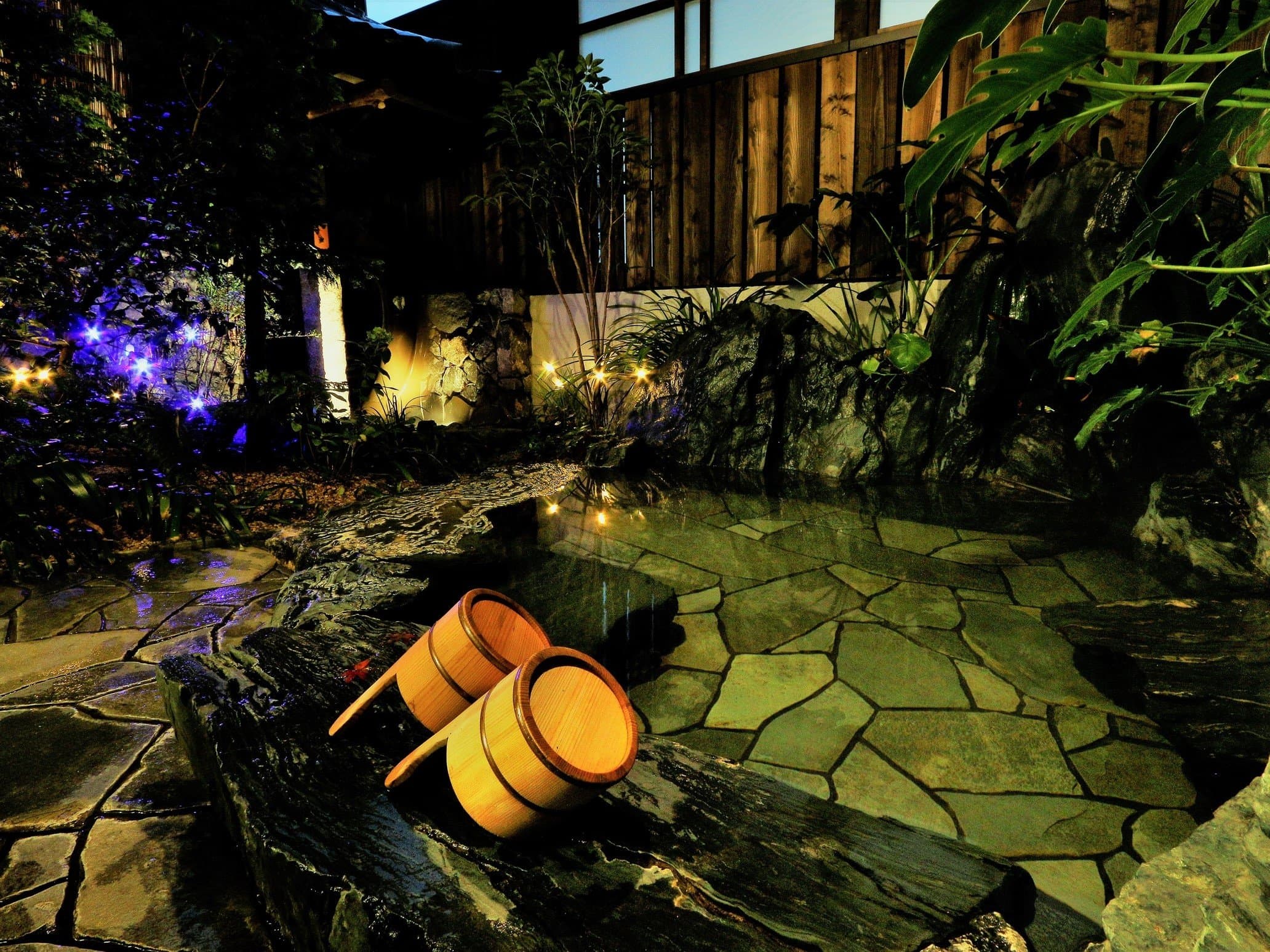 Outdoor rotenburo bath at Yado Taniya, Dogo Onsen, lit at night with stone paving and wooden bath buckets