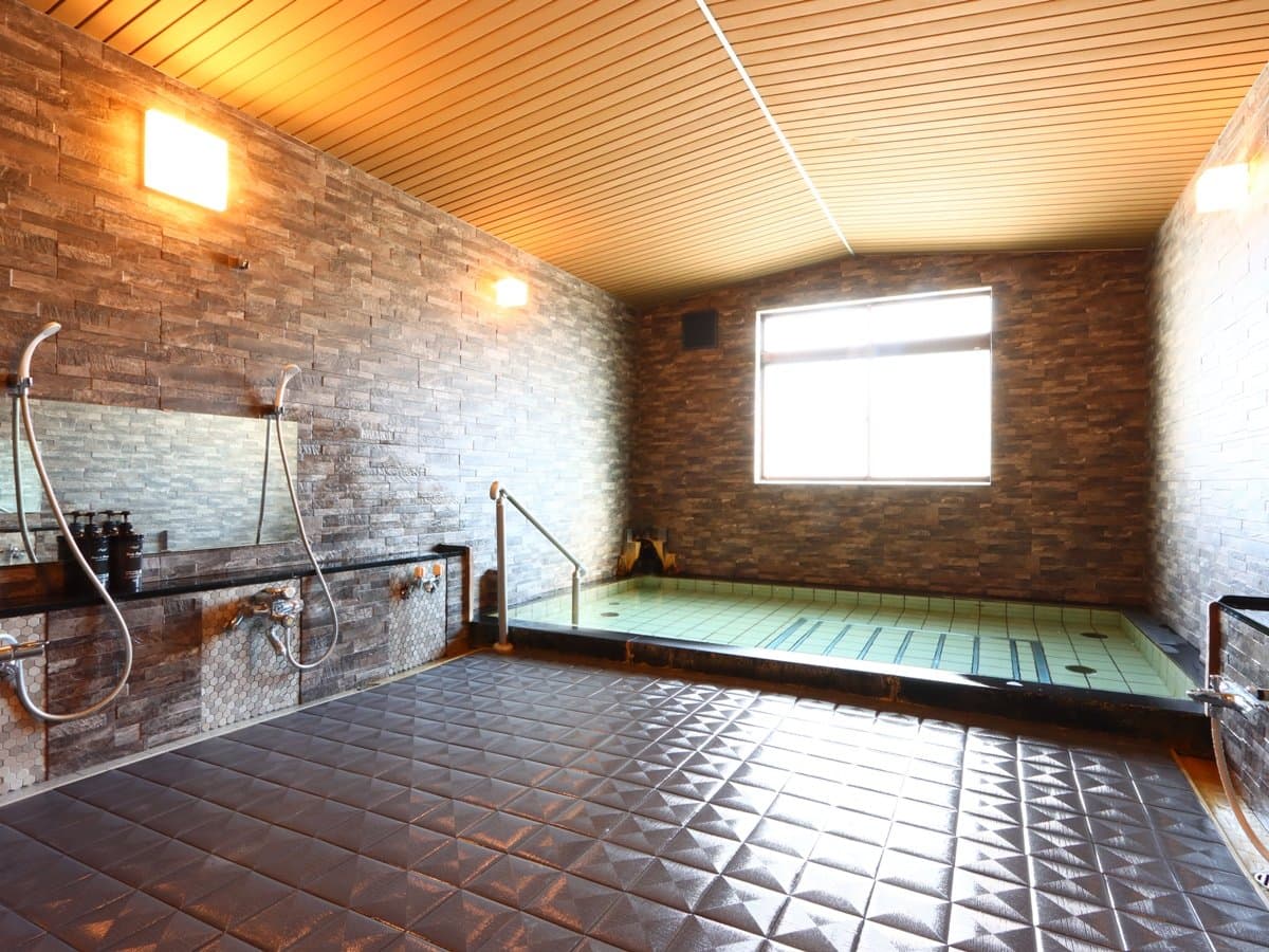 Indoor hot-spring bath with stone-clad walls and a tiled soaking tub at Hotel Cerulean Alpen, Tsugaike Onsen