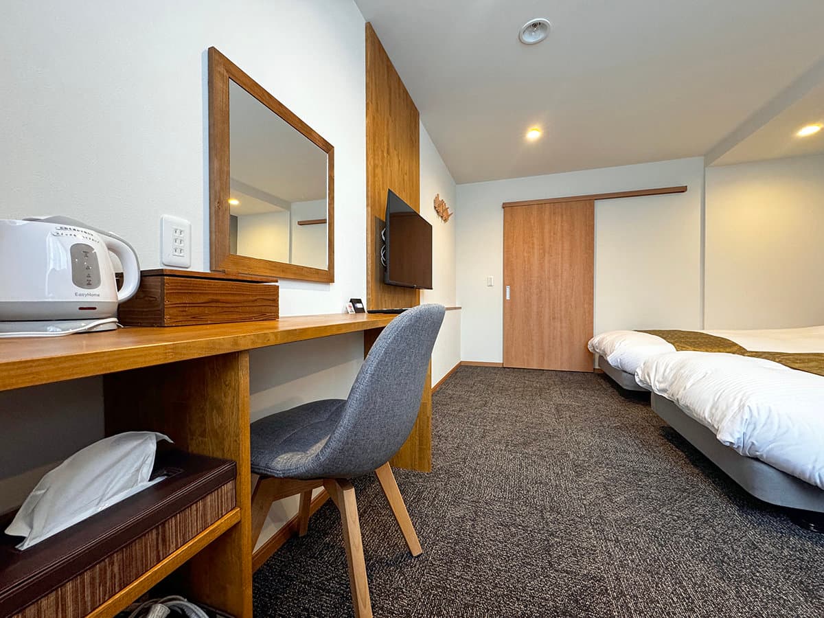 Modern Western twin guest room with wood desk, mirror and TV at Hotel Cerulean Alpen, Tsugaike Onsen