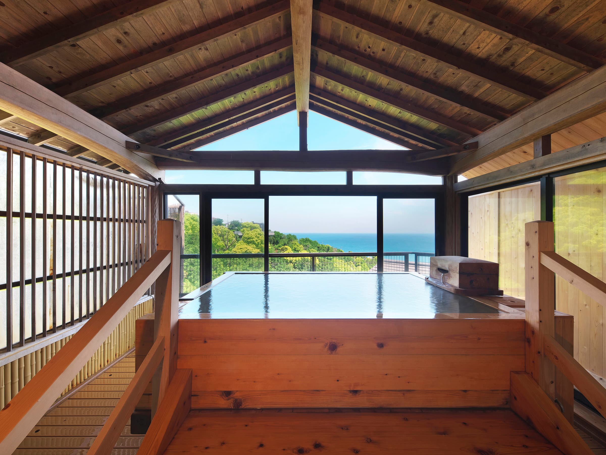 Wooden hot spring bath under a timber-framed roof with panoramic ocean view at Chikurinan Mizuno
